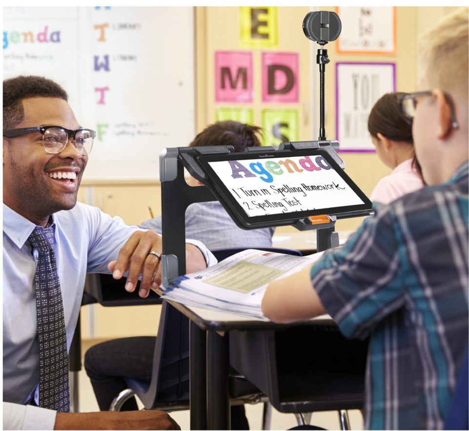 A teacher crouching down talking to a student using an electronic magnifier.