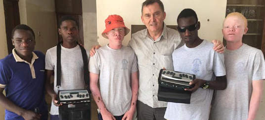 Group of five African students (two of whom have albinism) accompanied by one of our partners being photographed with their HumanWare devices.