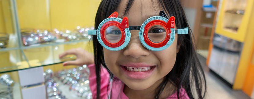 A school-aged girl taking a vision test at the optometrist with a smile on her face.