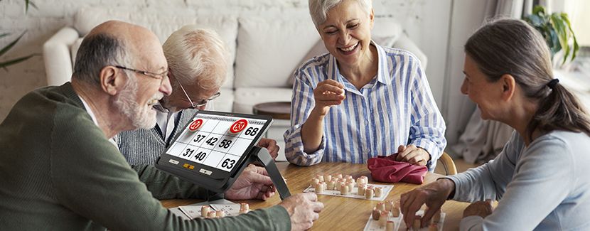 A group of seniors playing bingo with one of the people using the electronic magnifying glass explore 12 to see the numbers more clearly during the game. 