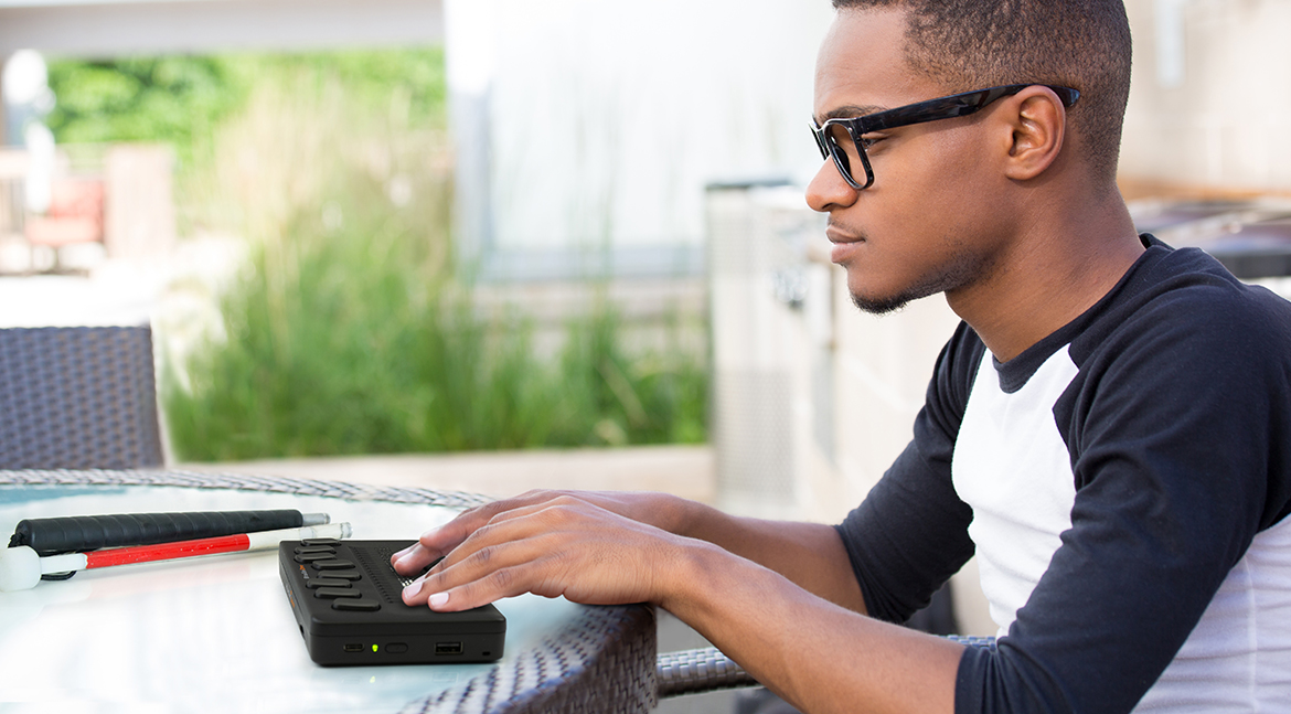 A blind boy wearing glasses and using BrailleOne outside. A blind boy wearing glasses and using BrailleOne outside.