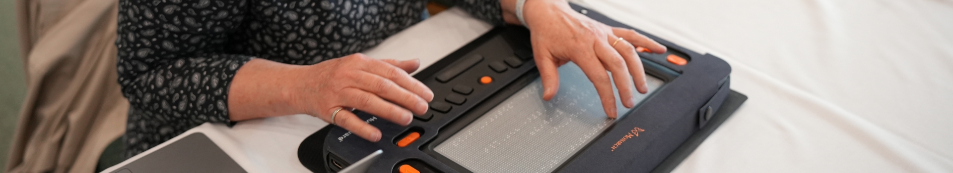 A hand touches a double line of dots to read braille on the Monarch's multiline tactile display.