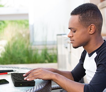 Image of a student sitting outside with his phone and white cane next to him, reading his emails with a Brailliant BI 20X.