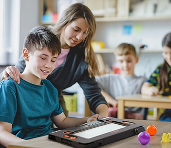 Image of a woman in a sweater helps a young boy use the Monarch on a table in a school library.