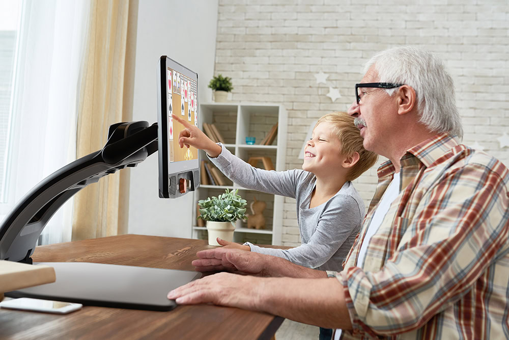 Portrait of a grandfather helping a happy little boy with his homework, seated at his desk and showing the blank screen of a Reveal 16.