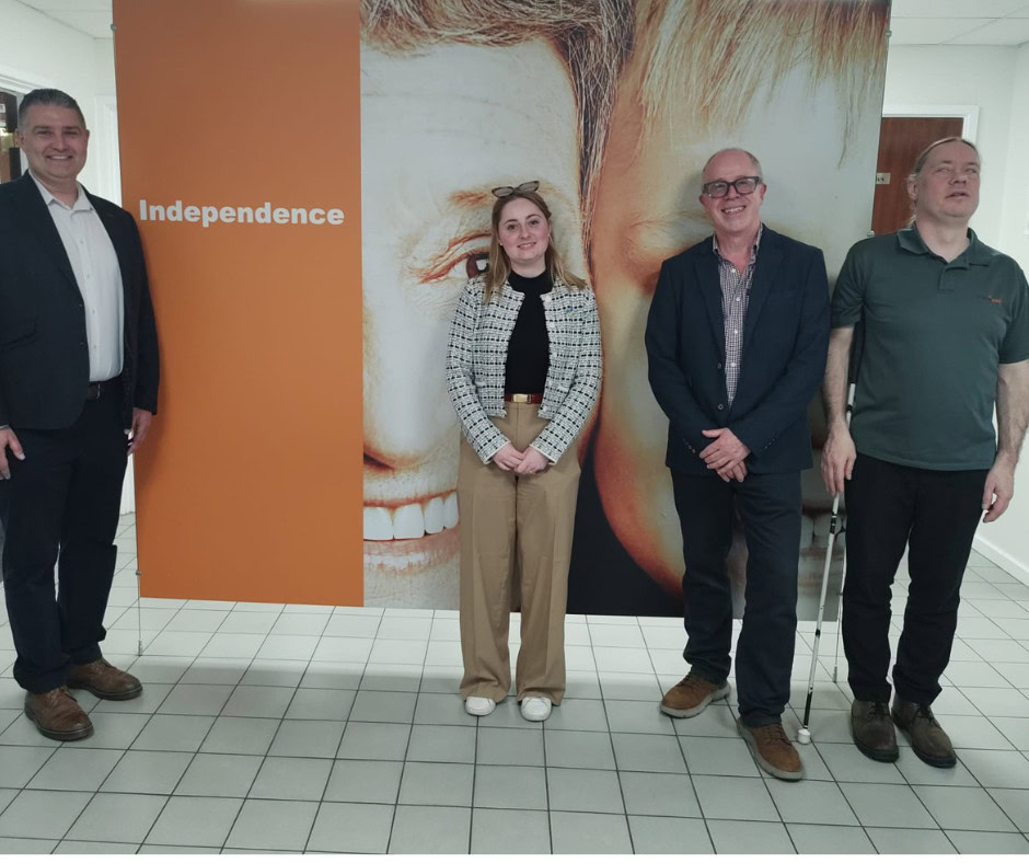 Chris, Gen, Alan et Martin à la réception de HumanWare, devant une grande affiche indiquant 