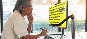 Image d’un homme lisant du texte sur son ordinateur, présentant du texte noir sur un fond jaune vif, créant un fort contraste.