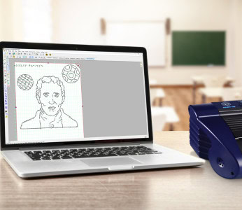 Image of a laptop displaying a dashed drawing, next to a Braille embosser.