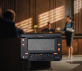 Image of a Monarch tactile tablet displayed prominently in the foreground, with a blurred courtroom scene in the background where a lawyer presents a case before a judge.