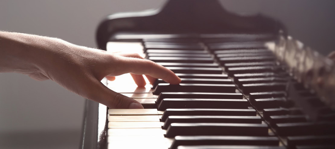 Hand playing the piano, white keys, black keys, surrounded by soft, warm light.