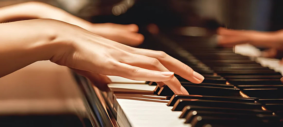 Close-up of a person's hands playing a piano, with soft lighting highlighting the fingers and keys.