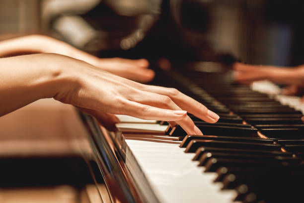 Close-up of a person's hands playing a piano, with soft lighting highlighting the fingers and keys.