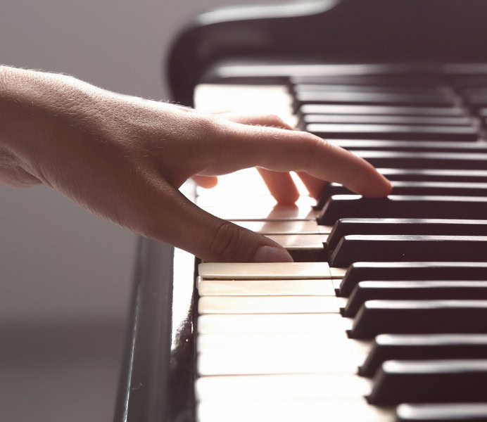 Main joue du piano, touche blanche, touche noire, environnée de lumière douce et chaleureuse.