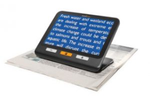 An Explore 8 electronic magnifier placed on newspapers, displaying enlarged text about the environmental challenges of climate change.