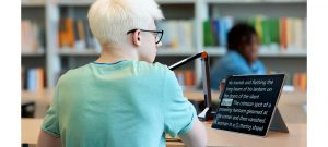 An albino student is reading a literary text on their tablet, seated in a library.