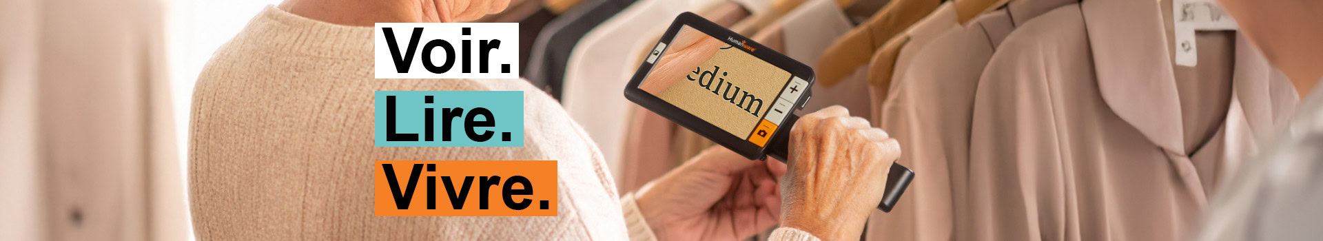 Personne utilisant une loupe numérique portative pour lire l’étiquette de taille "medium" sur un vêtement en magasin, avec le texte "Voir. Lire. Vivre."