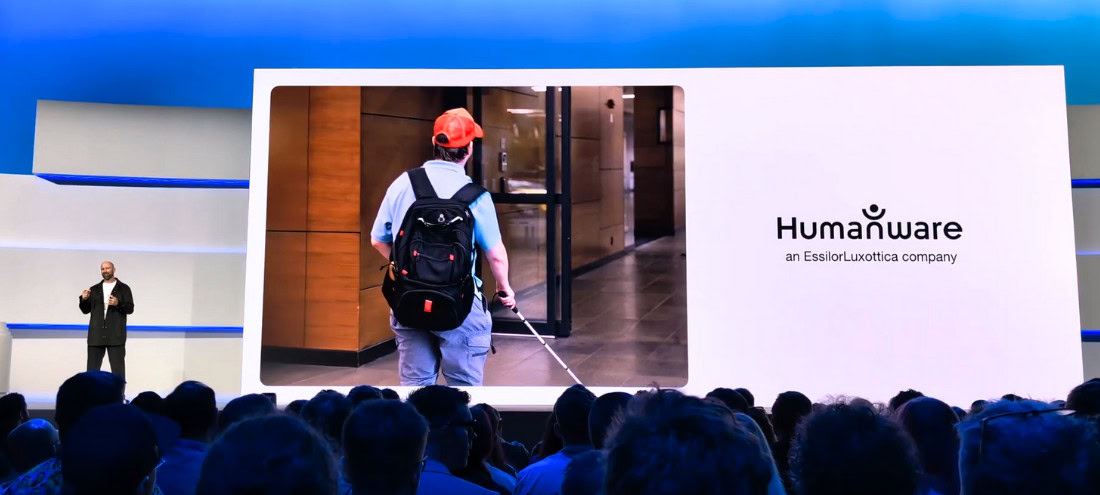 Humanware presentation at a technology event, where a speaker on stage shows a photo of a blind person entering a building with a white cane.