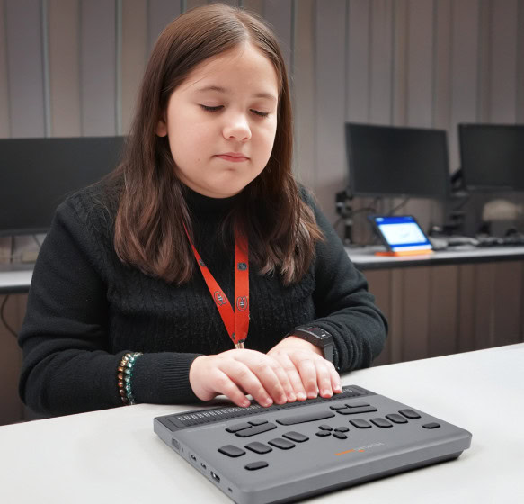 Young girl reading on a BrailleNote evolve in a classroom setting.