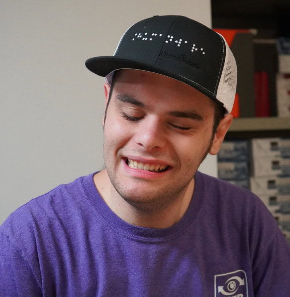 Young man smiling while wearing a HumanWare cap.
