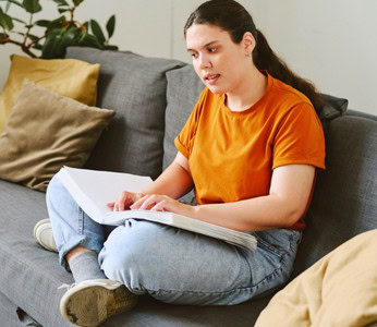 Young woman sitting on a couch reading a braille book.