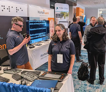Trade show booth for HumanWare showcasing assistive technologies, with several people talking and demonstrating products in an exhibition hall.
