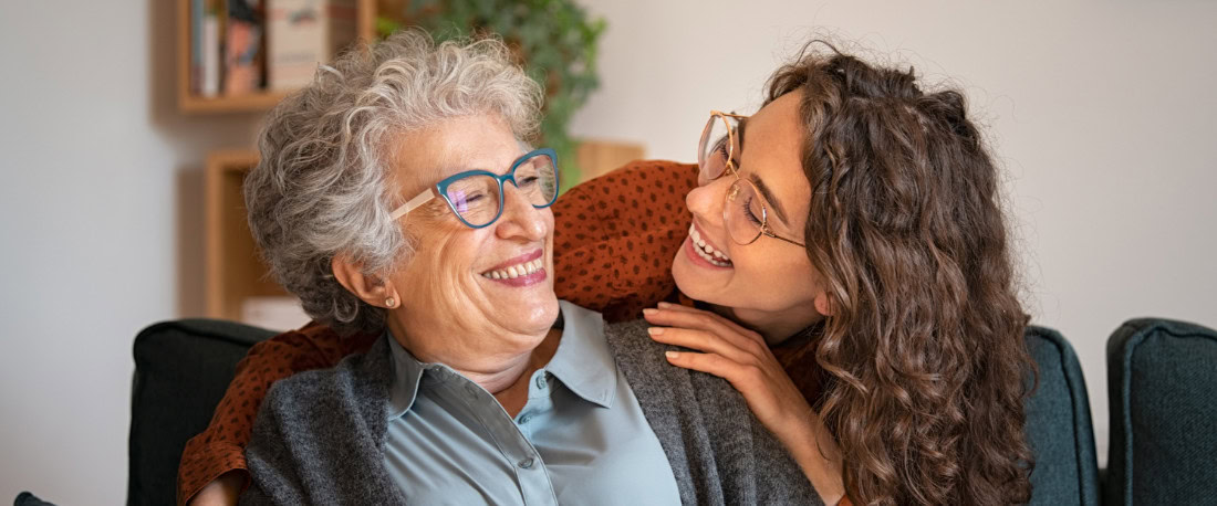 A young woman hugs an older woman, both smiling.
