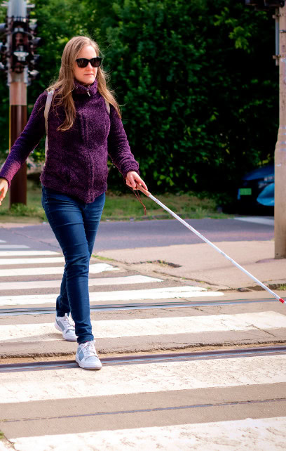Person crosses a crosswalk using a white cane. Person crosses a crosswalk using a white cane.
