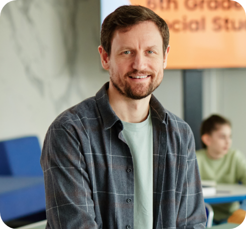 Smiling teacher in a classroom with students in the background.