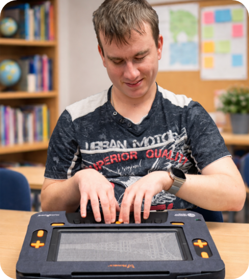 Young man uses a Monarch braille device in a classroom.