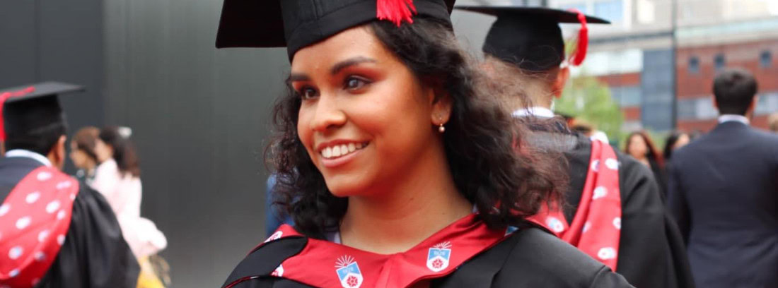 Jane smiling at her graduation ceremony, wearing a black and red gown and mortarboard.