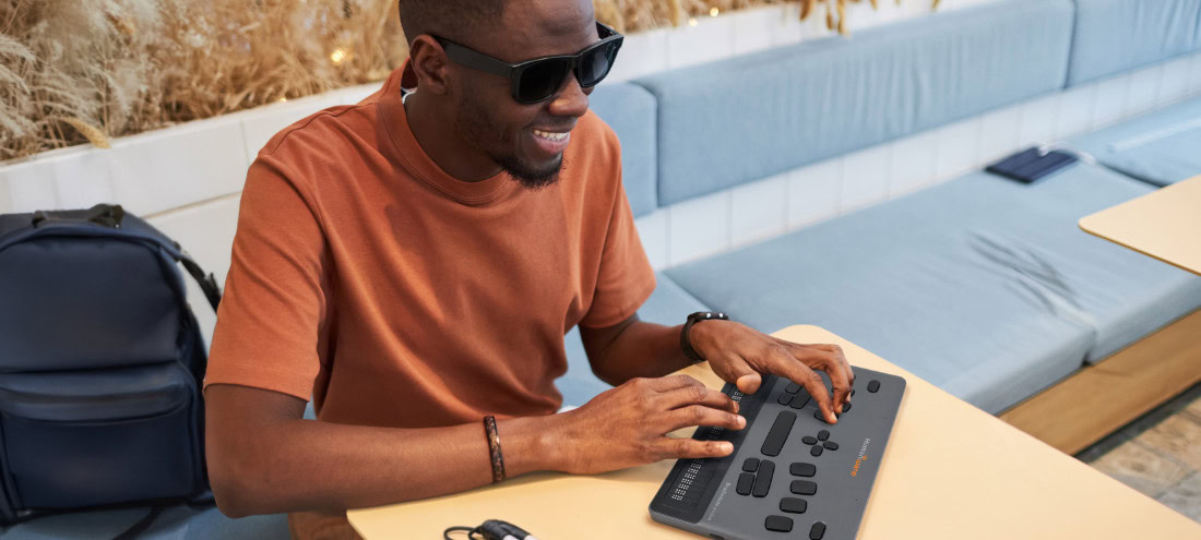 Blind professional working with the HumanWare BrailleNote evolve, a braille notetaker and computing device for work, education, and productivity.