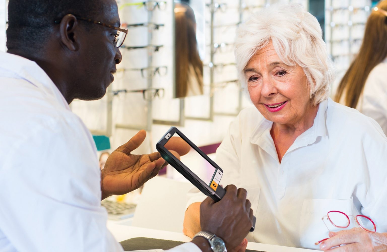 A professional helps an elderly woman by showing her an exploré 5 to improve her vision during a consultation.
